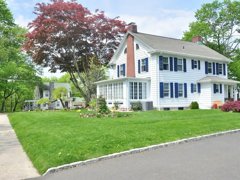 White colonial-style house with blue shutters and a front lawn